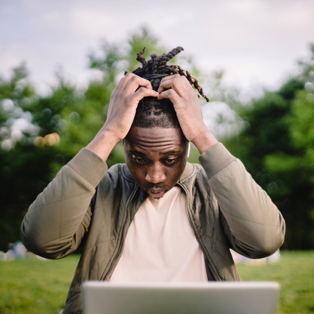 Man in khaki jacket running his hands through his hair, looking stressed by what is on the computer screen in front of him.
